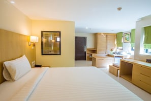 Habitación de hotel con una cama grande, un escritorio, un armario y un baño visible a través de una puerta.