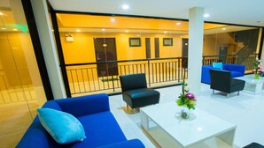 A modern lobby with a blue sofa, a black armchair, and a white coffee table with a vase of flowers. - Hotel on Hilltop (Kathu)