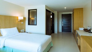 A hotel room with a large bed, a wooden headboard, a bedside lamp, a mirror, a wooden desk, and a bathroom door. - Hotel on Hilltop (Kathu)