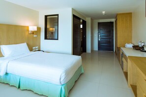 Habitación de hotel con una cama grande, cabecera de madera, lámpara de noche, espejo, escritorio de madera y puerta de baño.