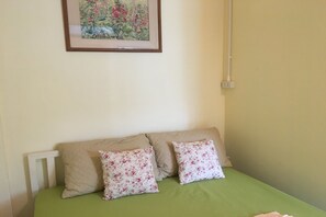 Un letto con lenzuola verdi e due cuscini floreali, una testiera bianca e un quadro con fiori appeso al muro.