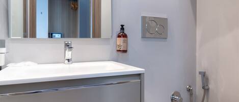 A modern bathroom with a white sink, a mirror, a toilet, and a shower.