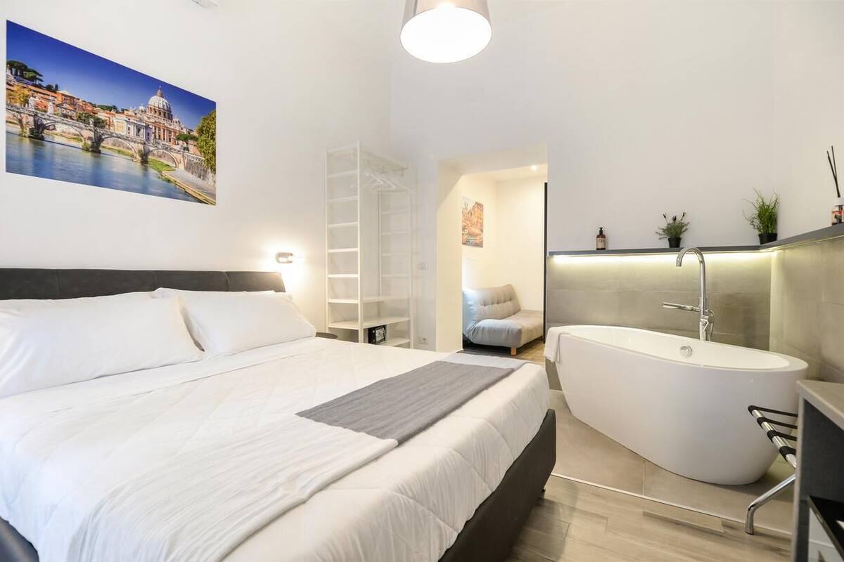 A modern bedroom with a large bed, a freestanding bathtub, and a view of a cityscape through a window.