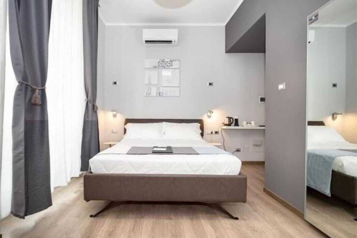 A modern bedroom with a large bed, bedside tables, an air conditioning unit, and a mirror.