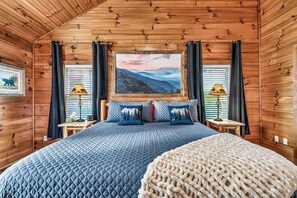 A wooden cabin bedroom with a bed, two nightstands, a painting, and a window with curtains. - Authentic Log Cabin • Pool Table • Near Dollywood • Easy Access (Pigeon Forge)