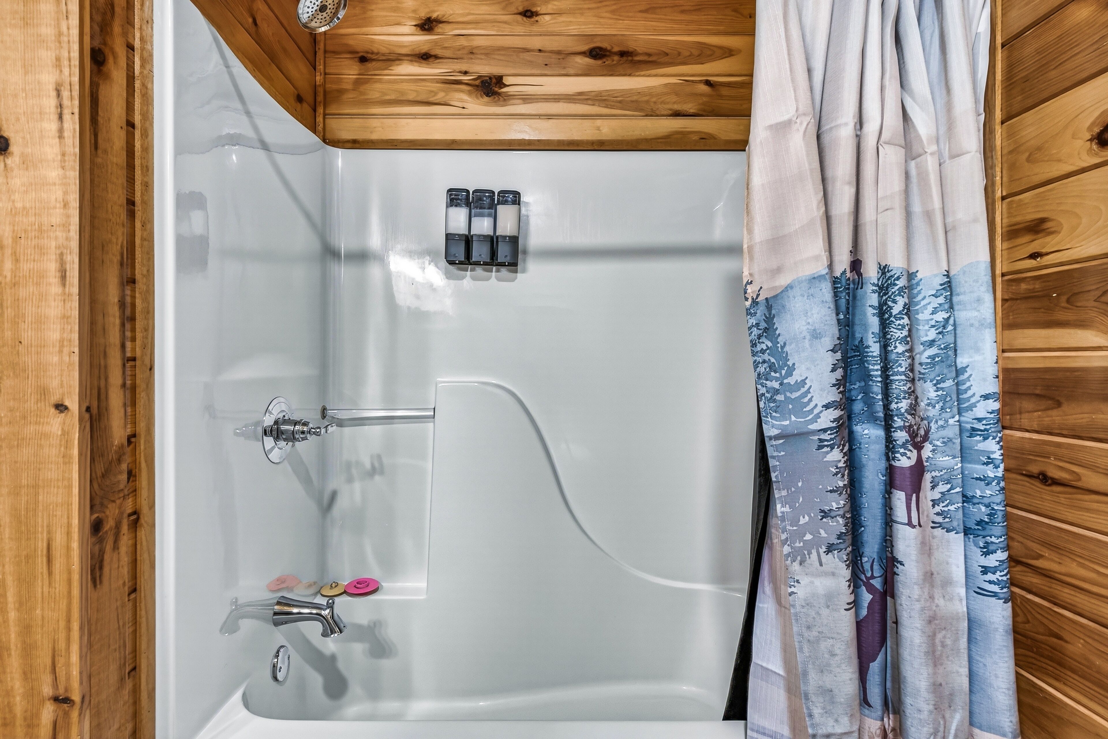 A shower with a wooden ceiling, a glass door, and a curtain with a forest design.