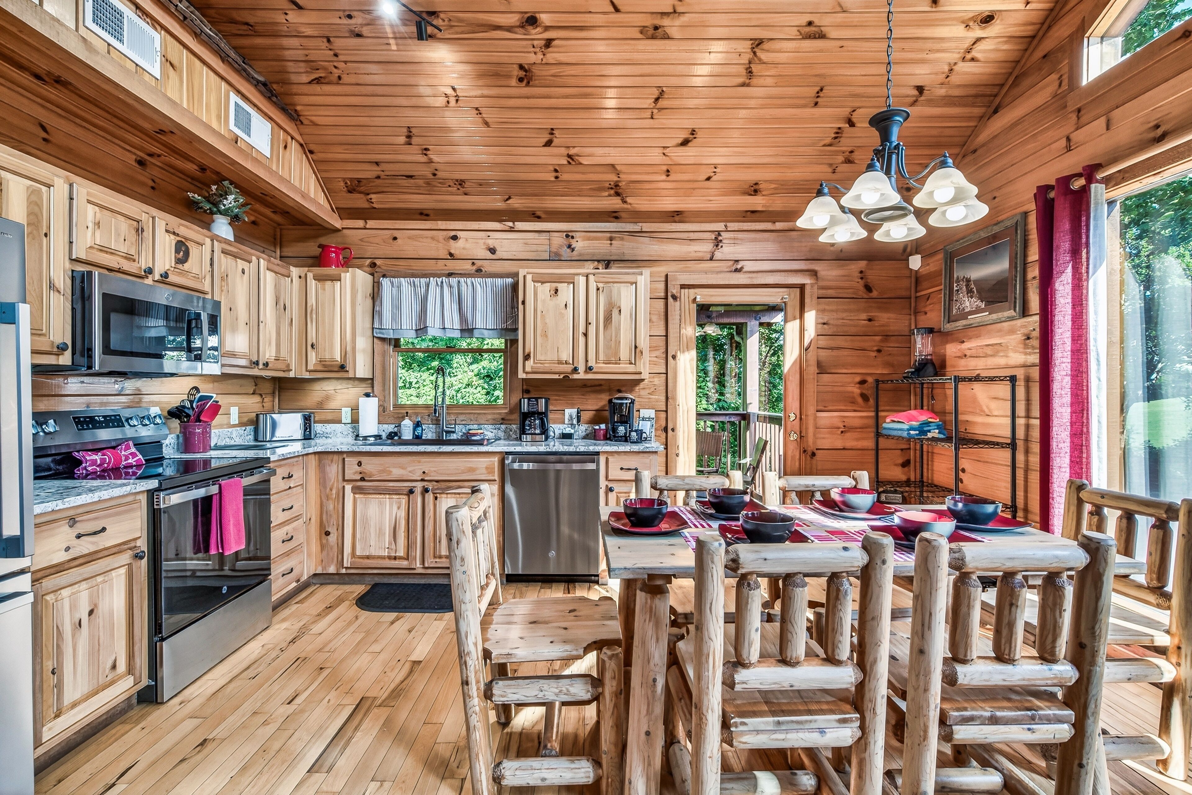 A wooden cabin with a kitchen featuring a microwave, stove, and dishwasher. There is a dining table with chairs and a chandelier.