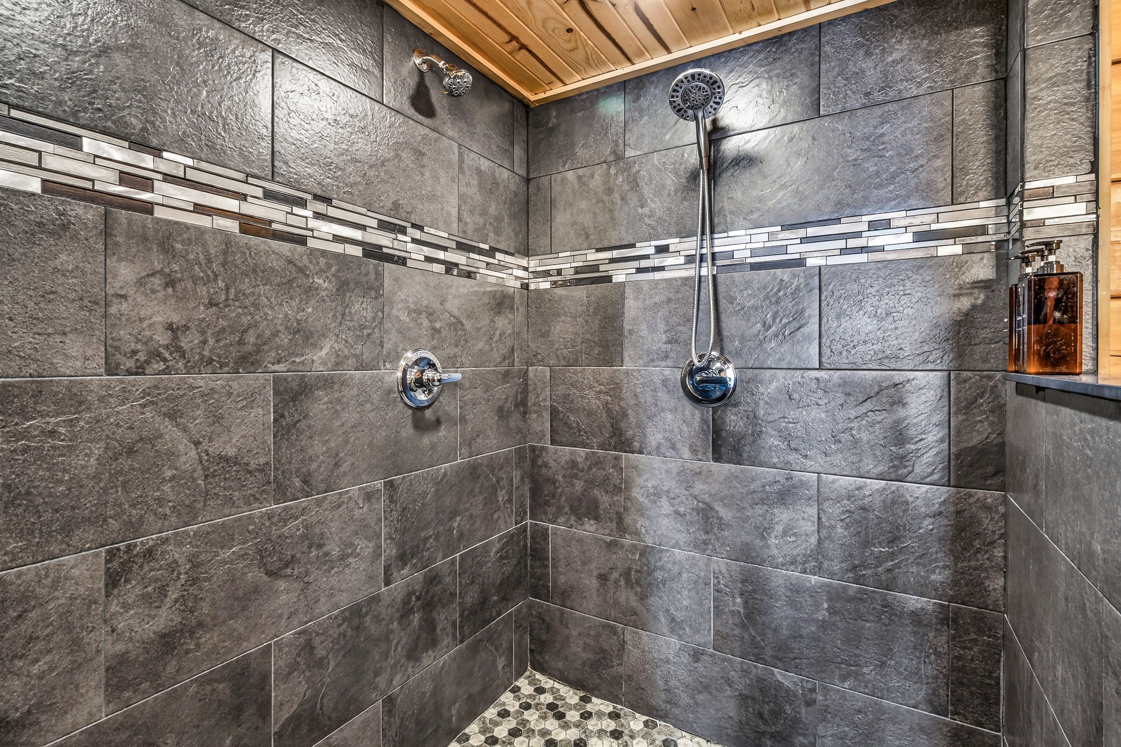 A shower with dark tiles and a wooden ceiling.
