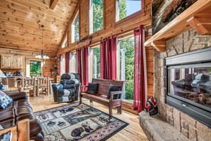 A log cabin interior with a fireplace, wooden furniture, and large windows. - Authentic Log Cabin • Pool Table • Near Dollywood • Easy Access (Pigeon Forge)