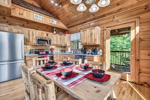 A wooden cabin with a kitchen, dining table, and a deck. - Authentic Log Cabin • Pool Table • Near Dollywood • Easy Access (Pigeon Forge)
