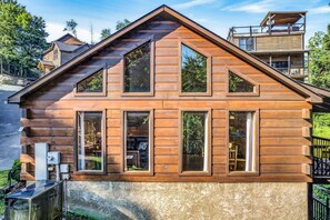 A wooden cabin with multiple windows, a sloped roof, and a small outdoor area with a grill. - Authentic Log Cabin • Pool Table • Near Dollywood • Easy Access (Pigeon Forge)