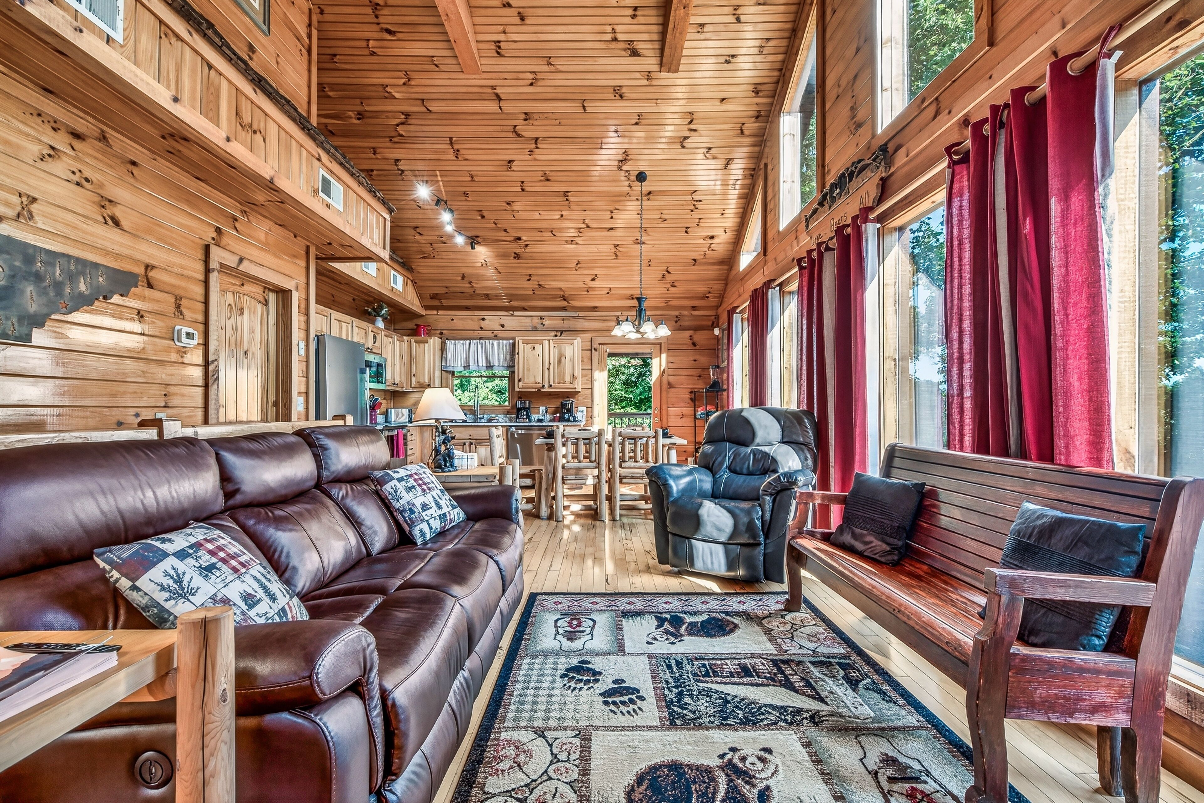 L’intérieur chaleureux d’un chalet avec un canapé en cuir, un banc en bois, un coin repas et de grandes fenêtres.