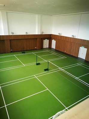 Ein Zimmer mit einem grünen, überdachten Tennisplatz, Holzwandverkleidung und Deckenventilatoren.