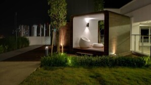 Un área lounge exterior moderna e iluminada, con un diseño minimalista, que incluye una zona de estar con una silla original de inspiración escultórica y una pequeña mesa.