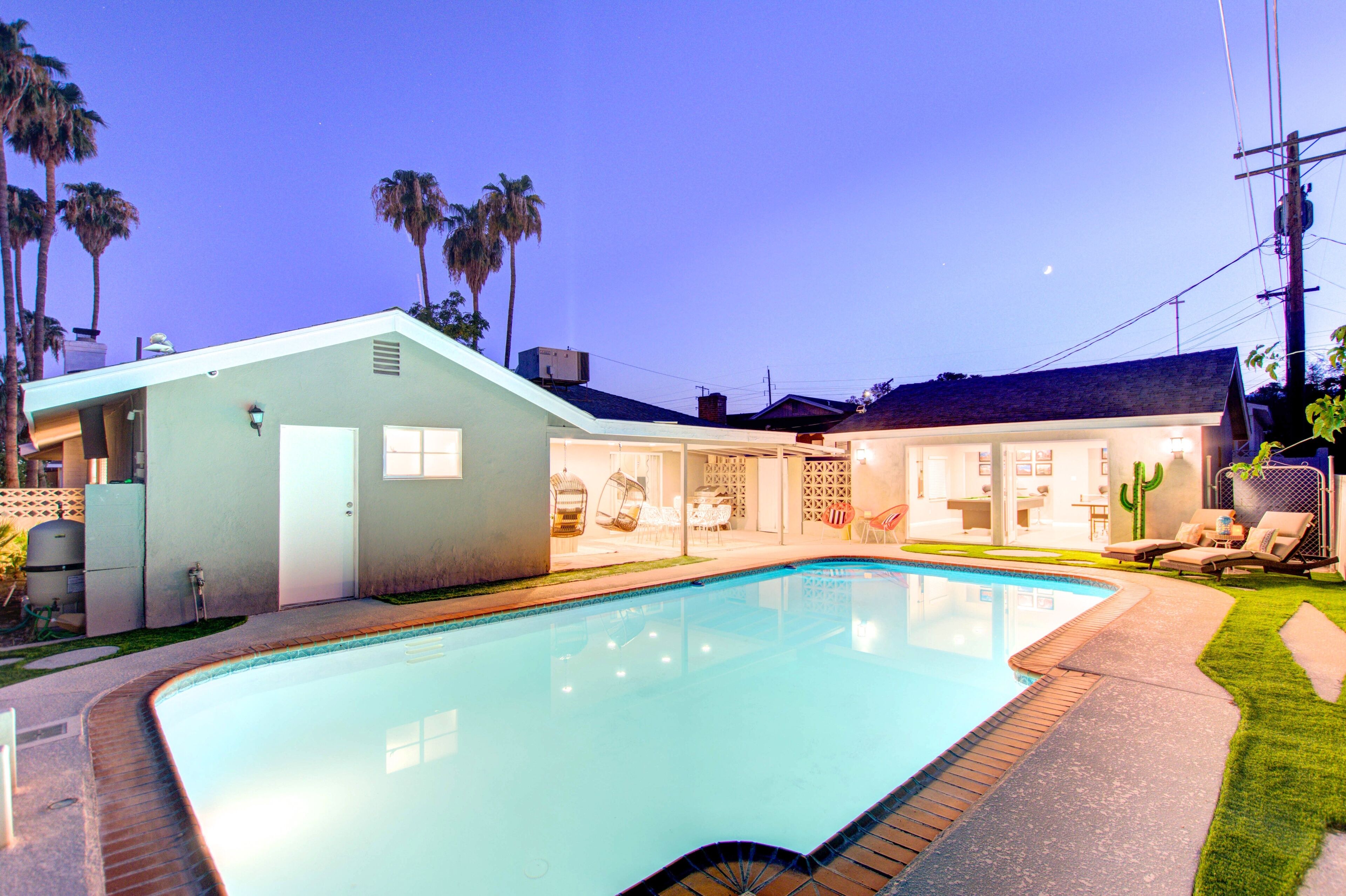 A modern house with a swimming pool, outdoor seating, and palm trees.