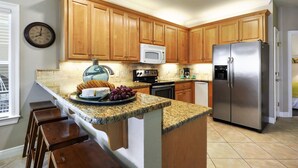 A kitchen with wooden cabinets, a stainless steel refrigerator, a microwave, and a granite countertop.