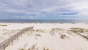A sandy beach with a wooden boardwalk leading to the water, a clear sky, and a calm sea.