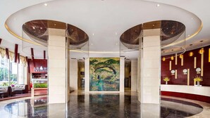 A spacious lobby with a large mural, a coffee shop, and a reception area with a clock and decorative plants. - Ramada by Wyndham Liuzhou Luzhai (Suzhou)