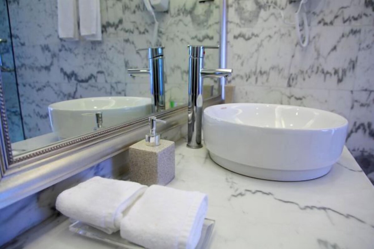 Un baño con un lavamanos blanco, dos grifos cromados, un salpicadero de mármol y un toallero con una toalla doblada.