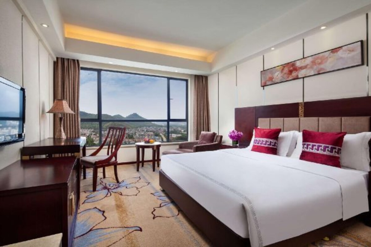 Ein Hotelzimmer mit einem großen Bett, einem Schreibtisch, einem Sessel und einem Fernseher.