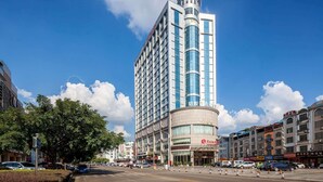 A tall hotel with a distinctive tower, multiple floors, and a curved facade. - Ramada by Wyndham Liuzhou Luzhai (Suzhou)