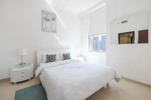 A modern bedroom with a large bed, a bedside table with a lamp, a window with a view of buildings, and a wall-mounted artwork. - DHH - Botanica Tower (Dubai)