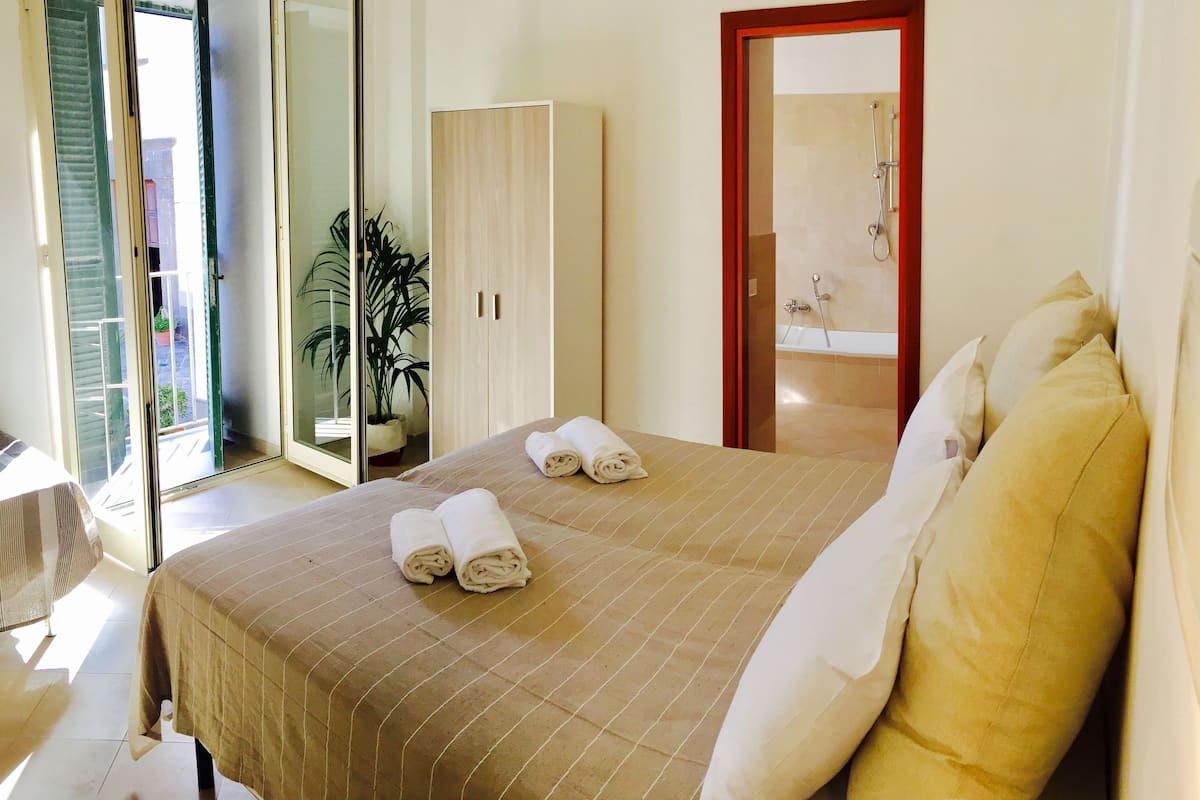A hotel room with a bed, a wardrobe, a bathroom with a shower, and a potted plant.