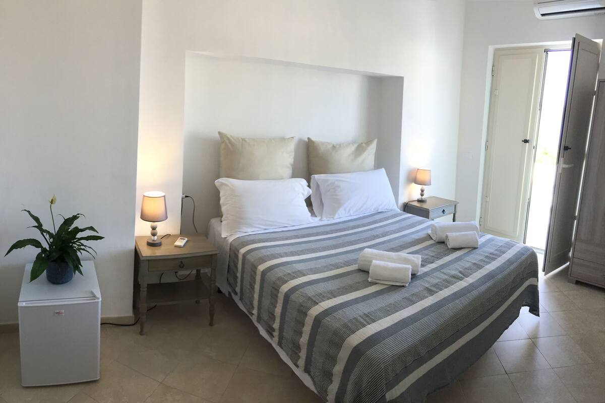 A neatly arranged bedroom with a bed, two bedside tables, a small refrigerator, and a potted plant.