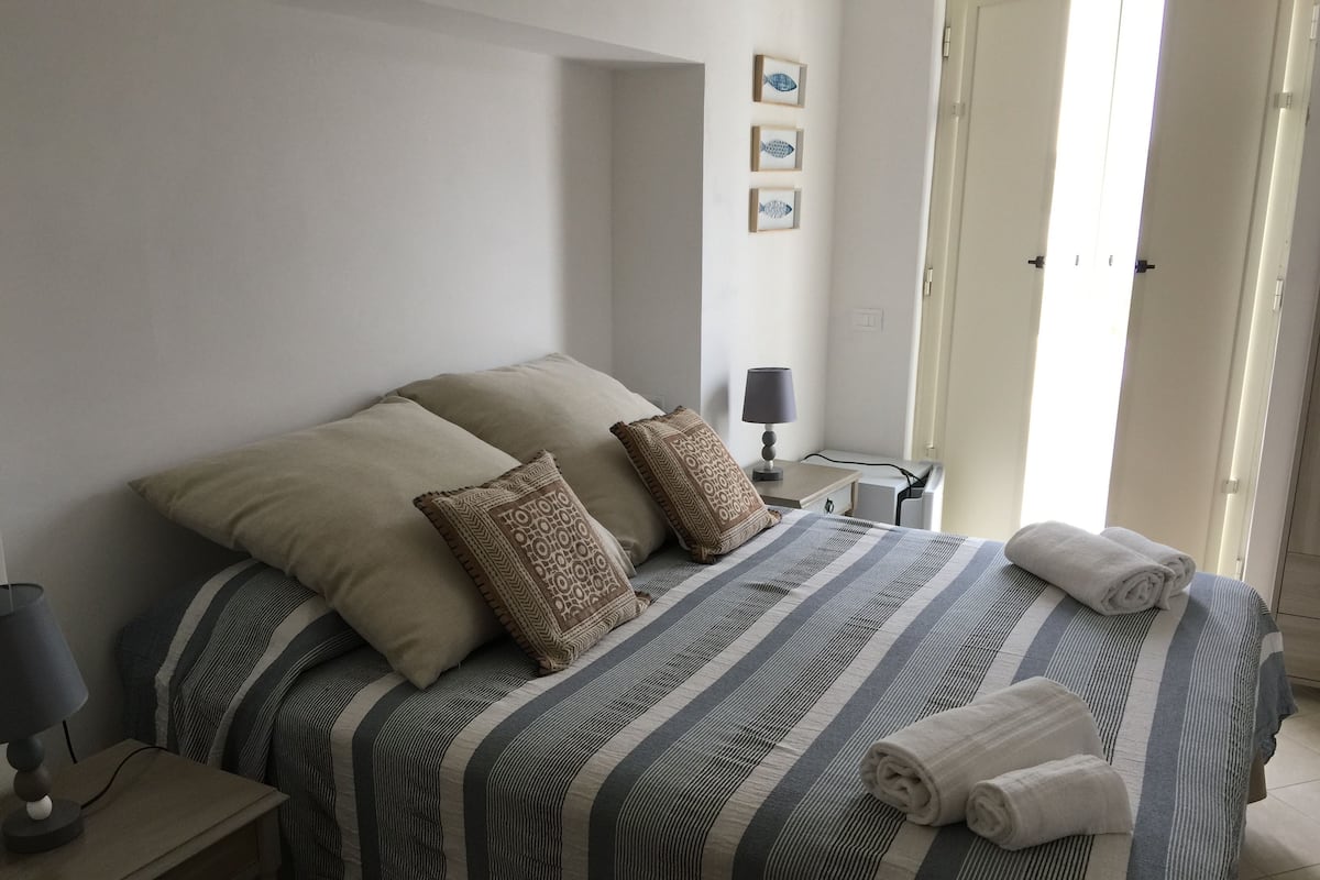 A neatly made bed with striped bedding, two pillows, and rolled towels on a nightstand.