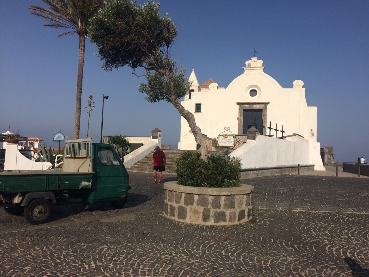 A white building with a dome and crosses, a green truck, and a palm tree.