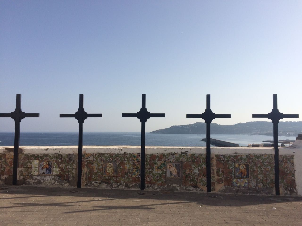 Blick auf die Küste mit einer Mauer, die mit Mosaikkunst und fünf schwarzen Kreuzen verziert ist.
