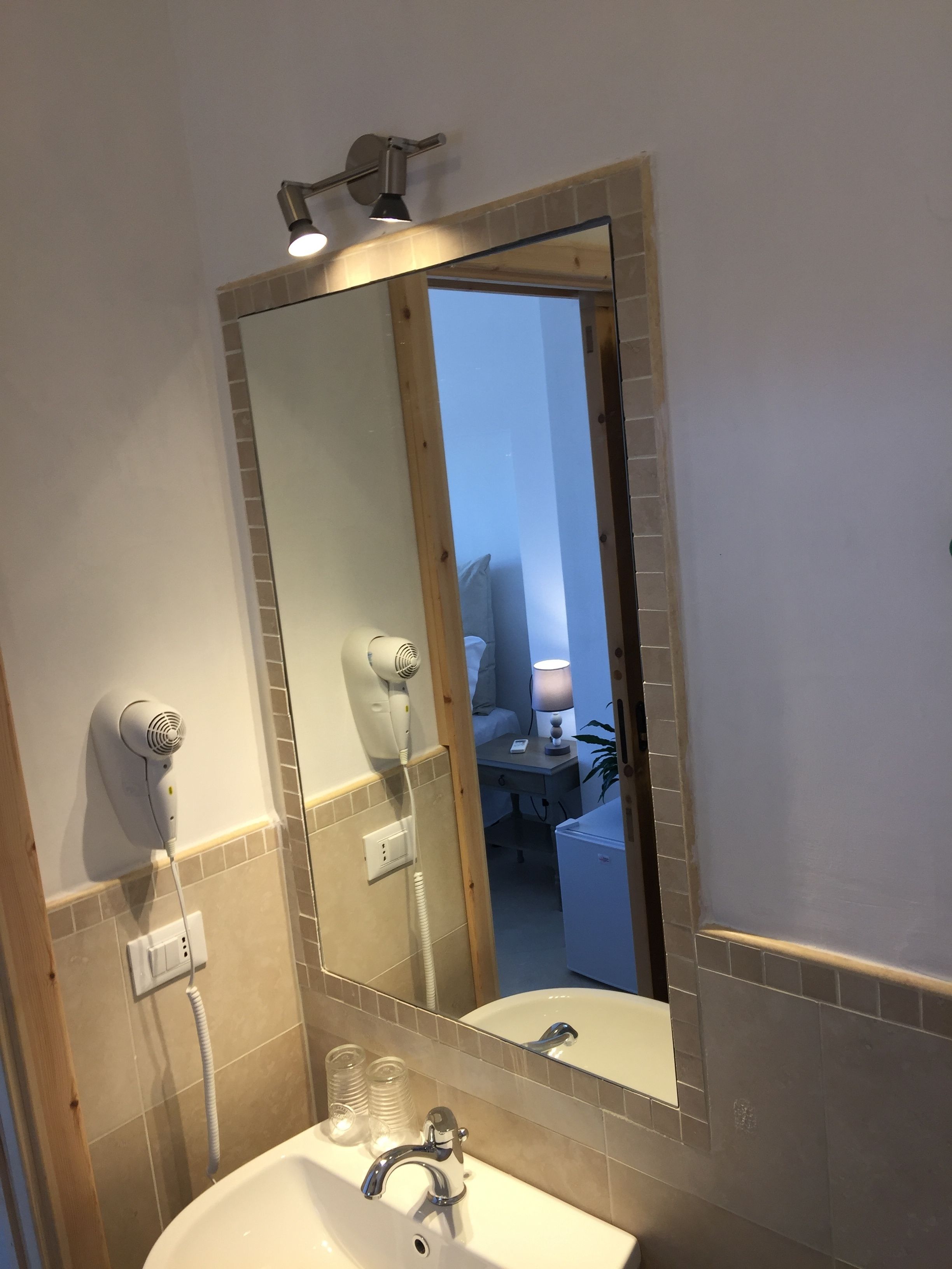 A bathroom with a large mirror, a sink, and a hairdryer mounted on the wall.