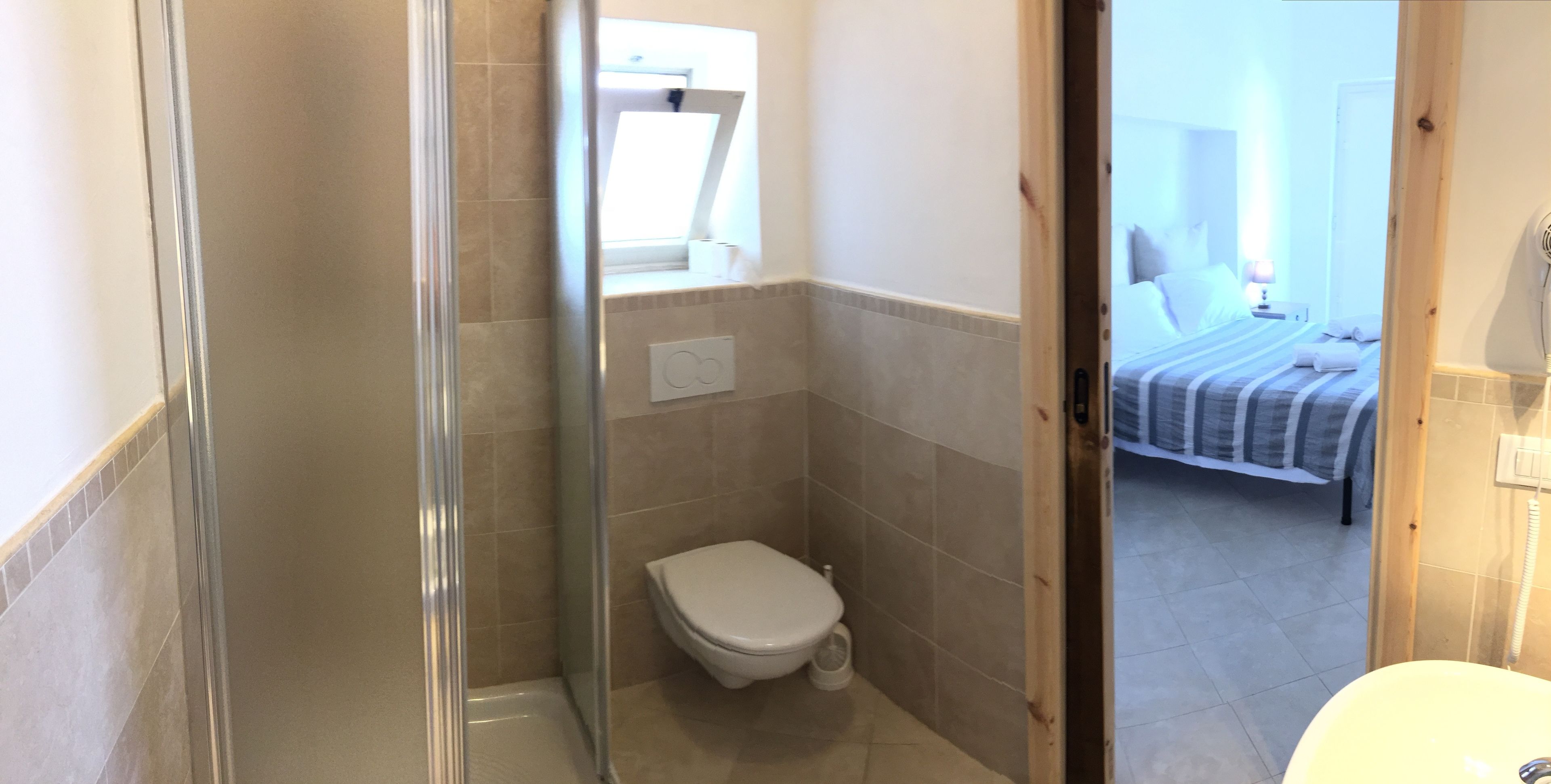 A bathroom with a shower, toilet, and a bed visible through an open door.