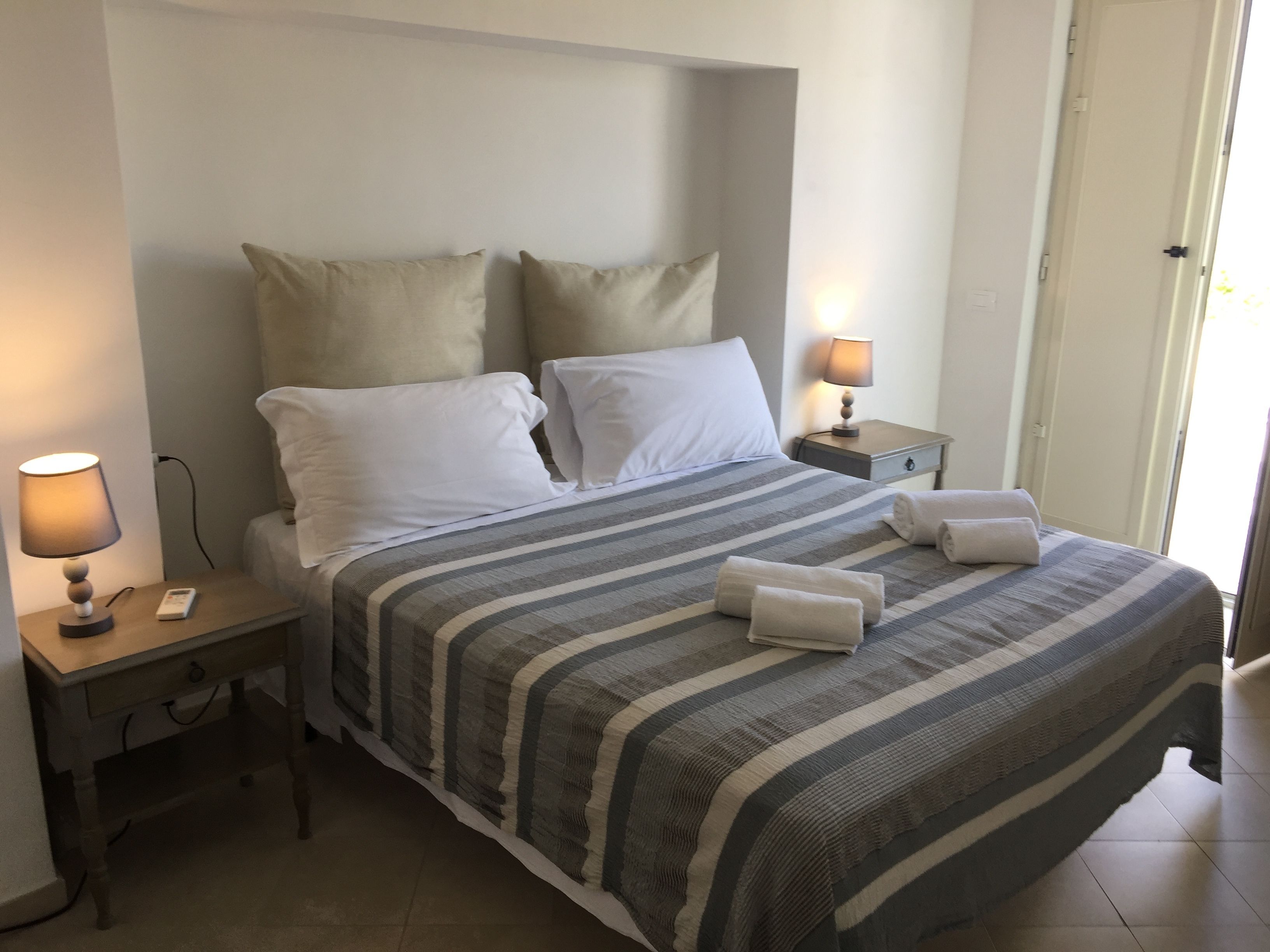 A neatly made bed with striped bedding, two bedside lamps, and a small bedside table with a remote control.