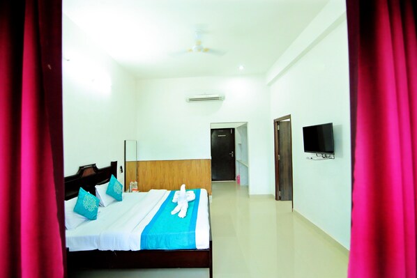 A hotel room with a bed, a television, and an air conditioning unit.