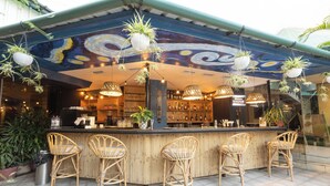 Zona de bar con sillas de mimbre, plantas colgantes y un mural en el techo.