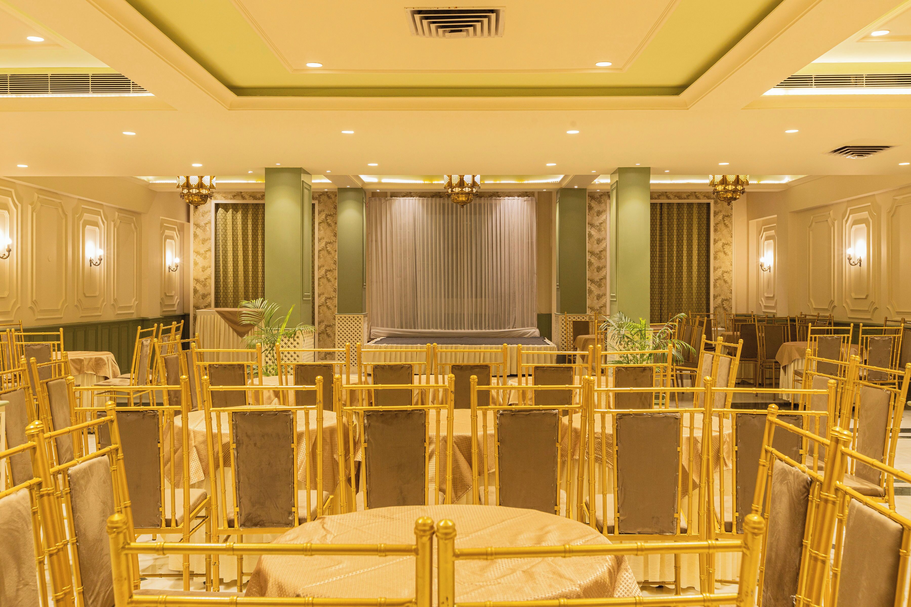 Un salón de banquetes con filas de mesas y sillas, un escenario e iluminación decorativa.