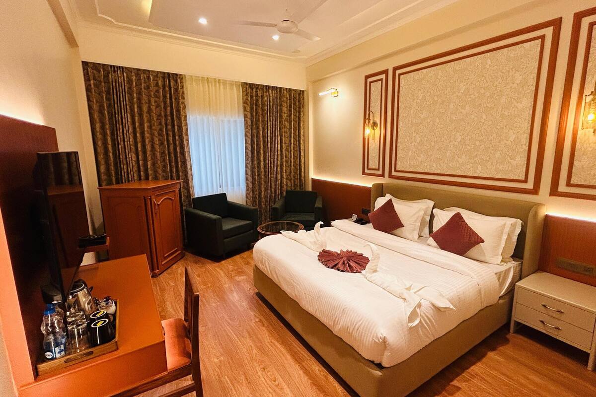 A hotel room with a large bed, a desk with a chair, a small table, and a wardrobe.
