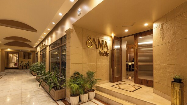 Entrada de hotel con piso de mármol, plantas en macetas y un cartel que dice 'SAMA HOTEL'.