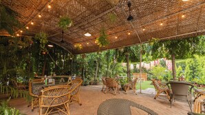 Un patio al aire libre con mobiliario de mimbre, plantas colgantes y techo de paja.