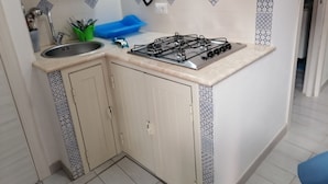 Une cuisine de taille réduite, équipée d’une cuisinière à gaz, d’un évier et d’un crédence décorée.
