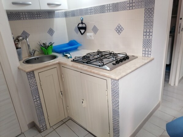 A compact kitchen with a gas stove, sink, and patterned backsplash. - Casa di Cecilia (Castellammare del Golfo)