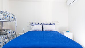 Un lit avec une couvre-lit bleue et des oreillers blancs, une table de chevet avec une lampe et une commode blanche.
