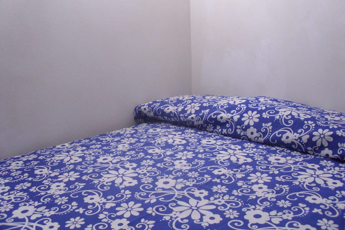 Ein Teil eines Zimmers mit einem Bett, das eine blaue, blumenmusterte Tagesdecke und passende Kissen hat.