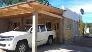 Een witte pick-up truck geparkeerd onder een houten overkapping bij een gebouw met een schotelantenne.