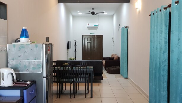 A compact kitchen with a refrigerator, kettle, and a blue water dispenser. A dining table with chairs is positioned in the center, with a sofa and curtains in the background. - Fahaz Taiping Homestay (Taiping)