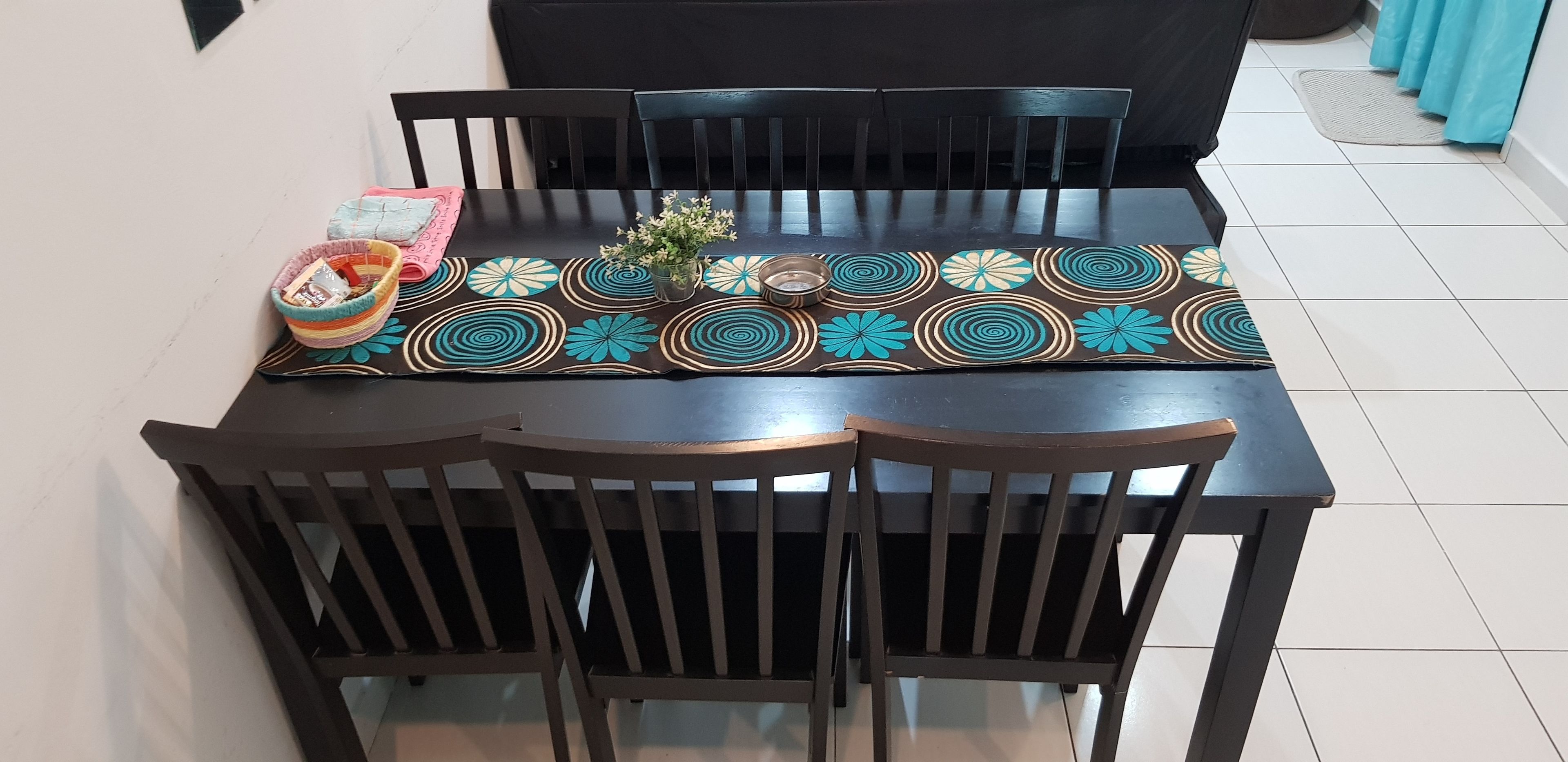 A dining table with a patterned table runner, black chairs, and a small potted plant.