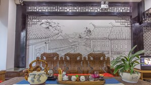 A traditional Chinese room with a large mural, a wooden chair, a table with tea set, and a potted plant. - The home of art and painting (Lijiang)