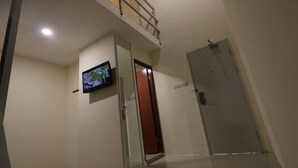 Un pasillo con un televisor montado en la pared, una puerta de vidrio y una puerta cerrada.