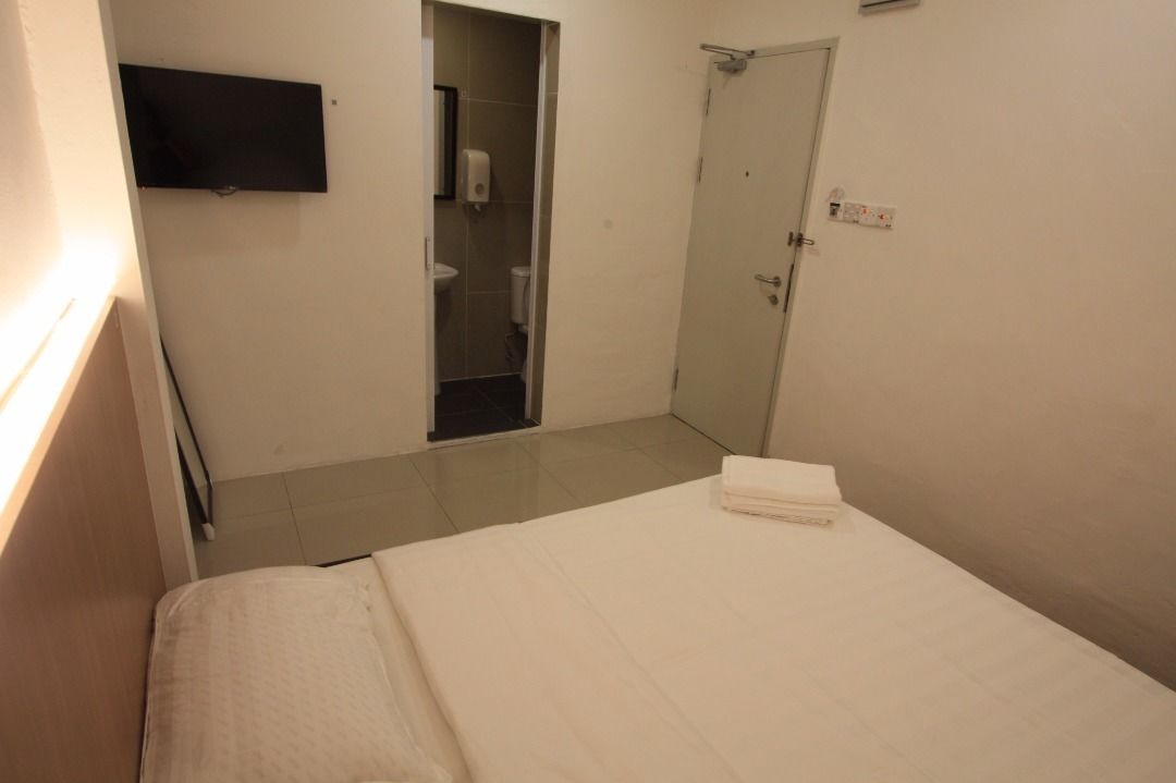 A hotel room with a bed, a TV mounted on the wall, a door, and a small bathroom visible through an open door.